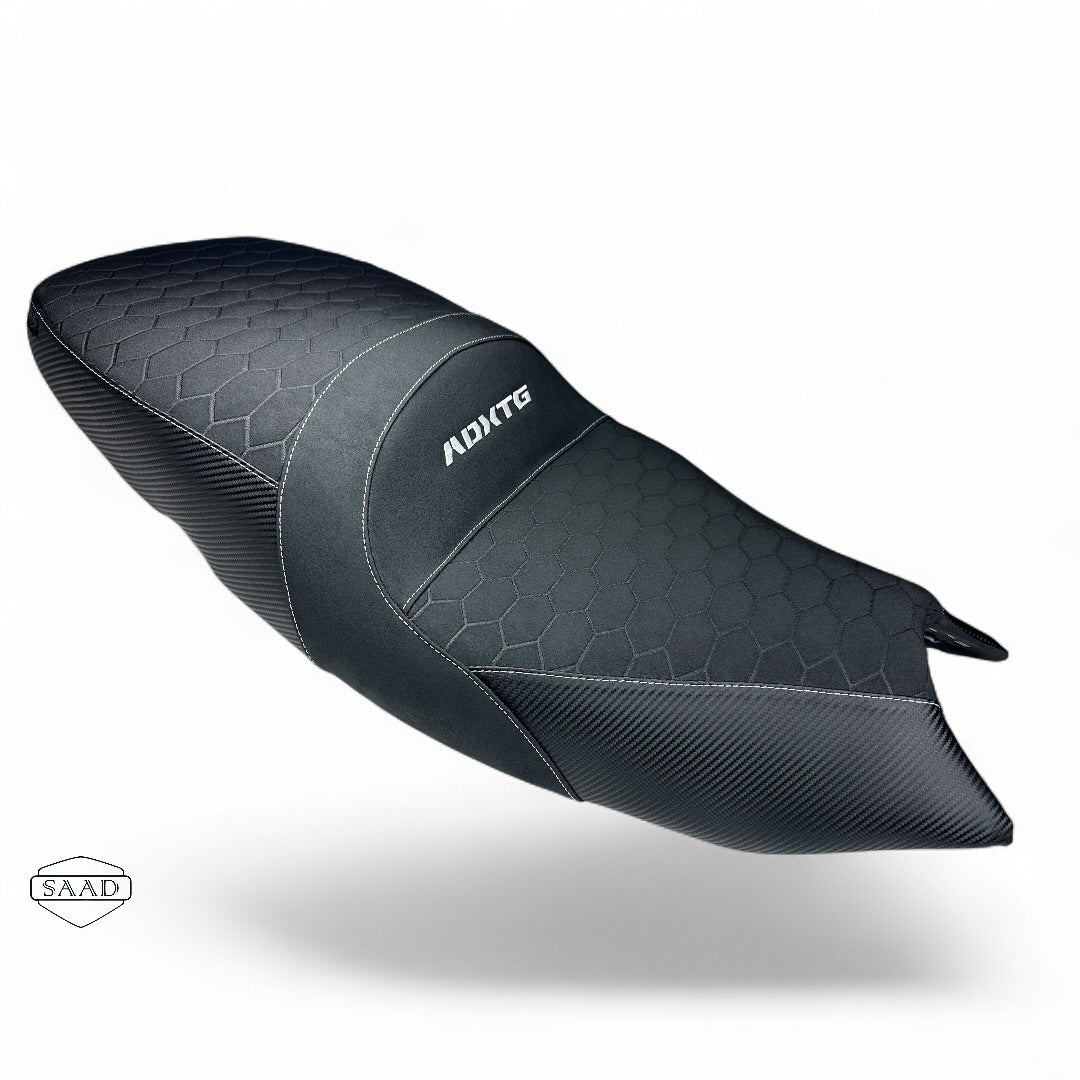 A black motorcycle comfort seat  with a carbon fiber weave pattern and a honeycomb texture, featuring the brand logo  'ADXTG' on the side